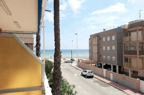 Een gebouw aan de kust met uitzicht op zee, een straat met auto's en een palmboom.