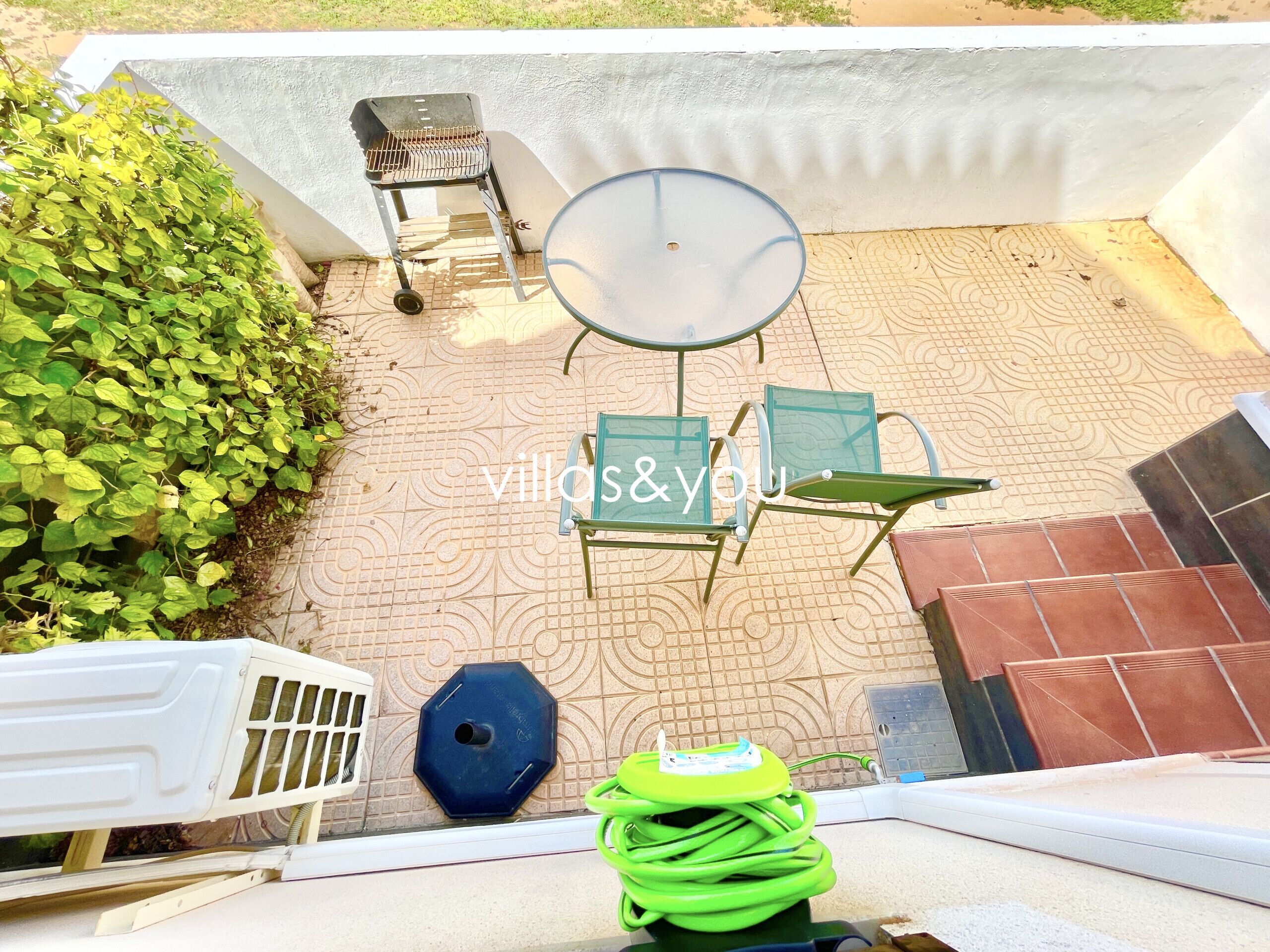 Een terras met een tafel, stoelen, een barbecue en een tuinslang.
