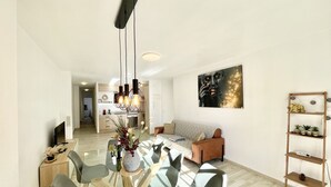 A modern living room with a dining area, a kitchen in the background, and a bookshelf. - Sunset Torrevieja by Villas&You (Torrevieja)