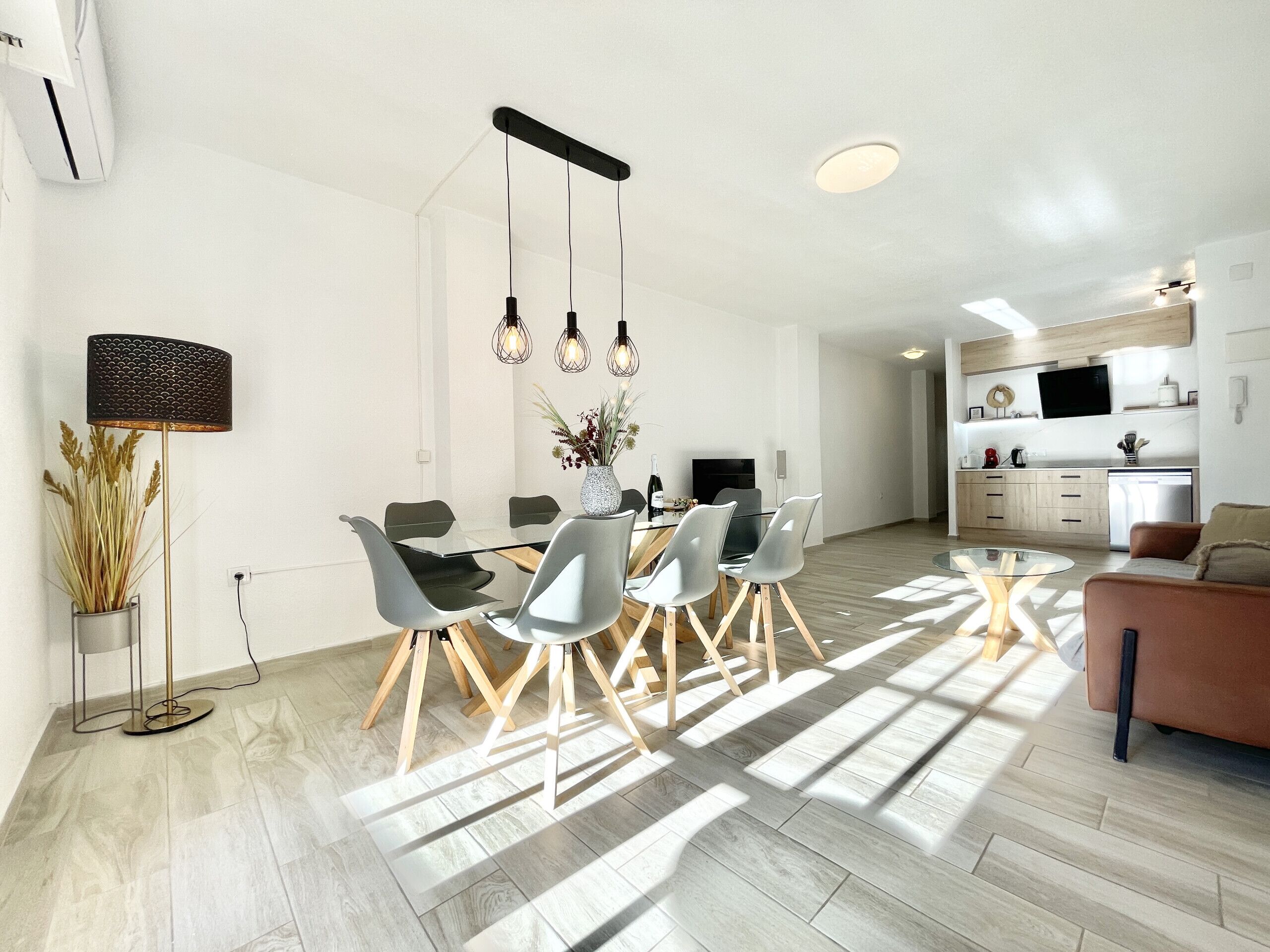A modern kitchen with a built-in oven, a dining area with a glass table and chairs, and a living room with a sofa and a coffee table.