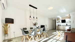 A modern kitchen with a built-in oven, a dining area with a glass table and chairs, and a living room with a sofa and a coffee table. - Sunset Torrevieja by Villas&You (Torrevieja)