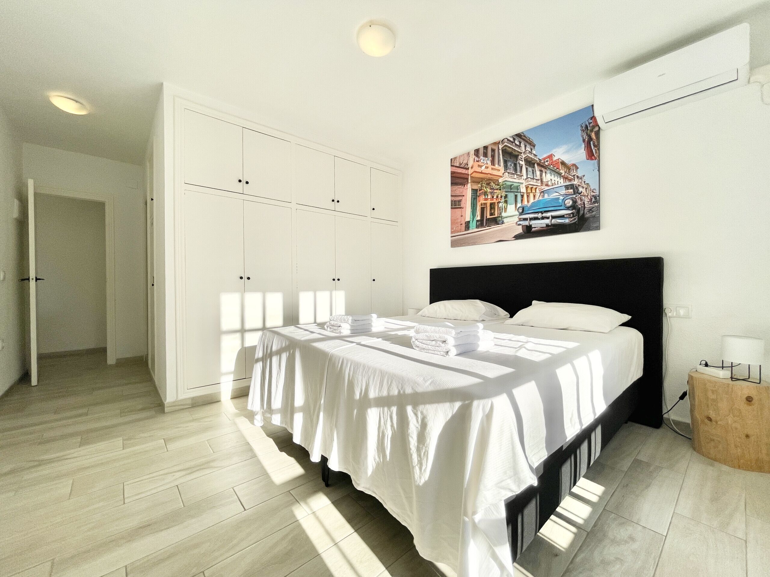 A bedroom with a bed, white wardrobe, and a painting of a street scene.