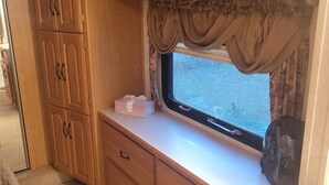 A compact kitchen with wooden cabinets, a window with curtains, and a small countertop.