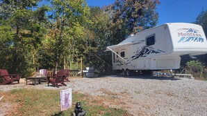 A recreational vehicle (RV) with a mountain design, parked in a campsite with a grill and seating area.