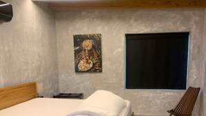 Un dormitorio con cama de madera, un ventanal grande, un cuadro colgado en la pared y una lámpara de pie.
