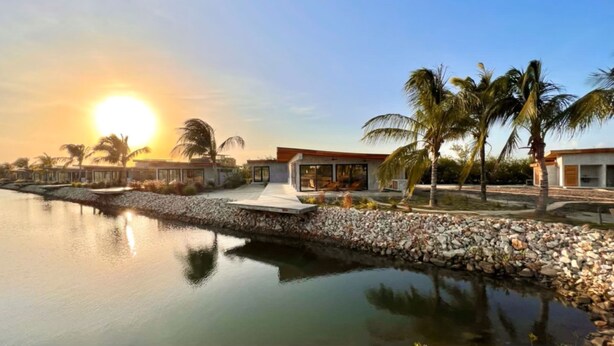 Un resort moderno con piscina, palmeras y vista al atardecer.