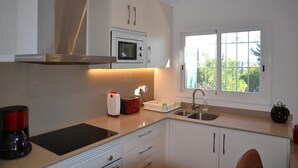 A modern kitchen with white cabinets, a stainless steel range hood, a built-in microwave, a coffee maker, and a window with a view of greenery. - Las Palmeras 5 - L'Estartit, Torre Gran (Estartit (L´))