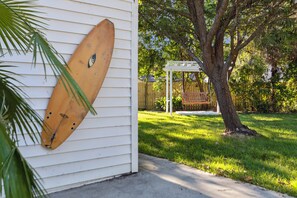 Enjoy the coastal vibe with a surfboard mounted on the exterior wall, surrounded by an outdoor space with a pergola and lush surroundings.