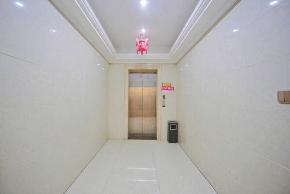 A hallway with a tiled floor, a trash bin, and an elevator. - Junlan Hotel (Xiangyang)