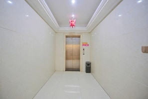 A hallway with a tiled floor, a trash bin, and an elevator.