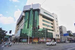 A multi-story building with a modern glass facade, a crosswalk, and traffic lights at a street intersection. - Junlan Hotel (Xiangyang)