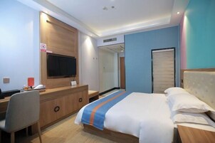 Una habitación de hotel con cama, escritorio, silla, televisor y espejo.