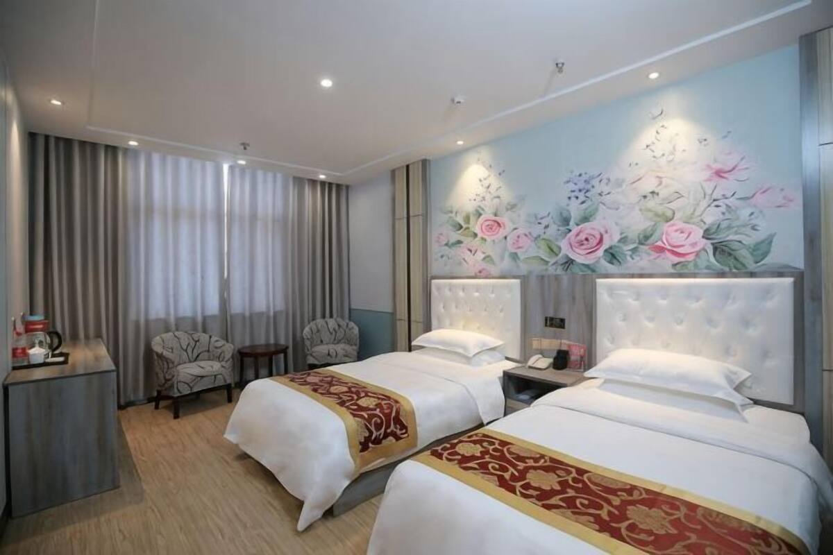 A hotel room with two beds, a desk, a chair, a nightstand, and a floral mural on the wall.