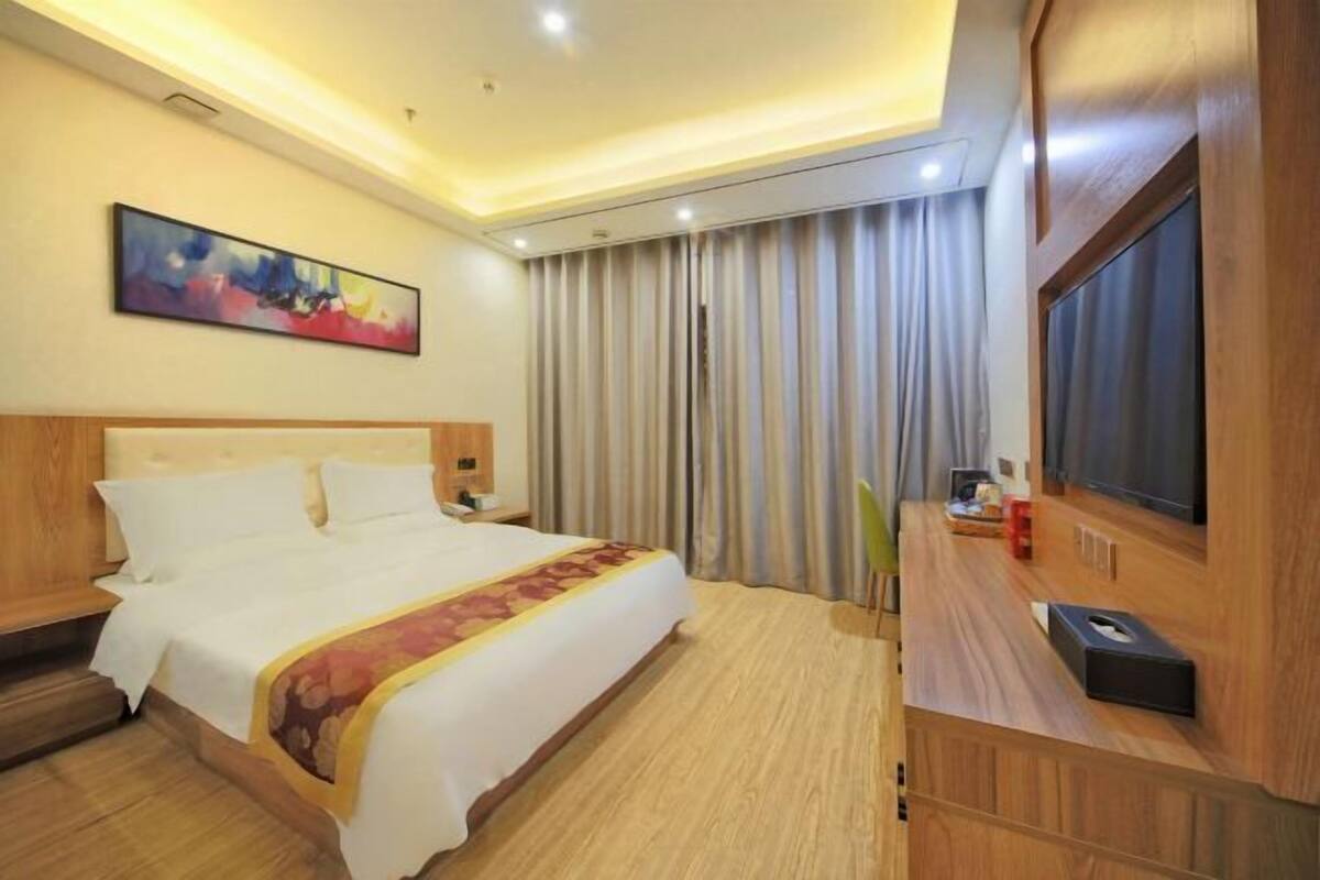 A hotel room with a large bed, a flat-screen TV, a wooden headboard, and a painting on the wall.