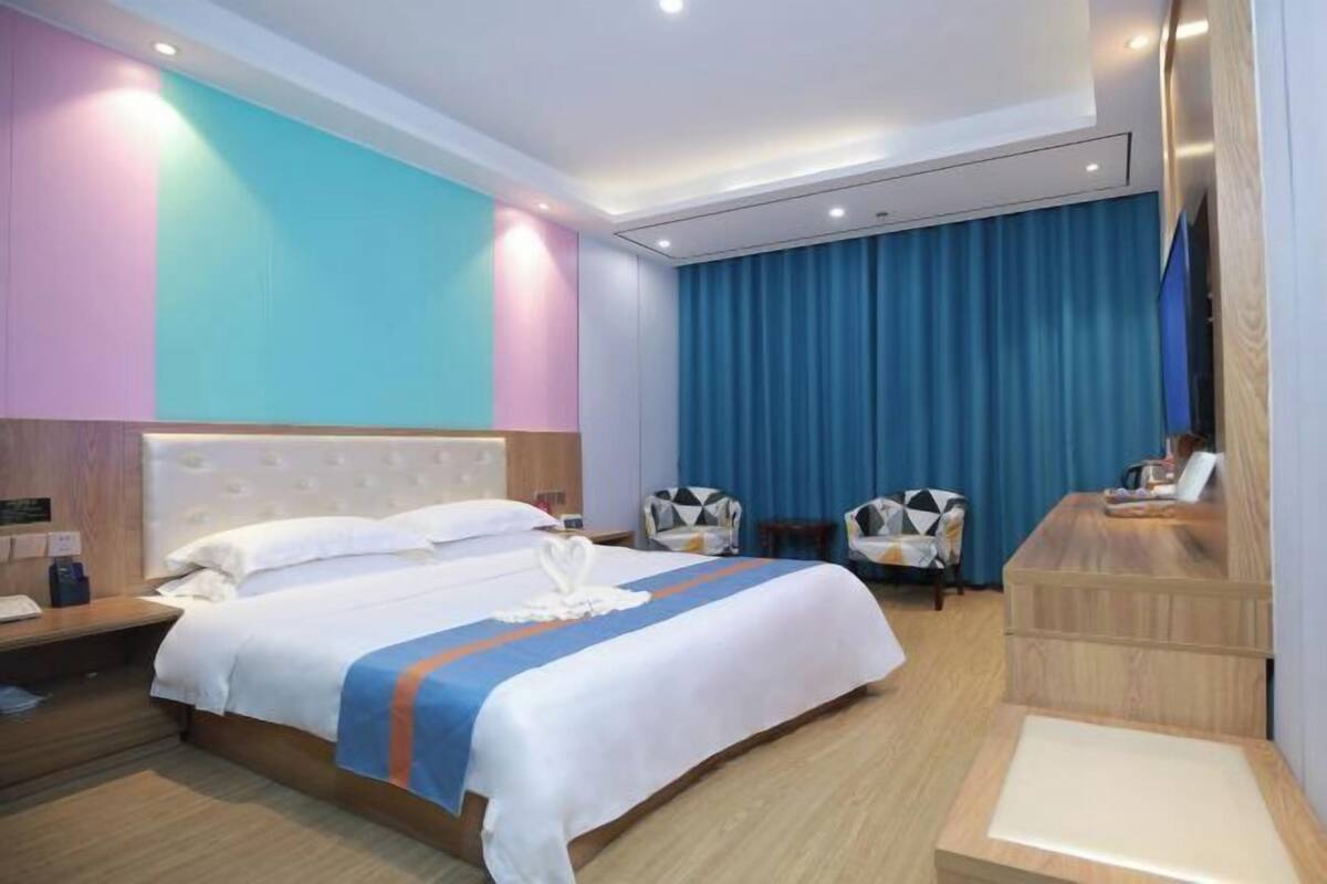 A hotel room with a bed, a desk, two chairs, and a blue curtain.