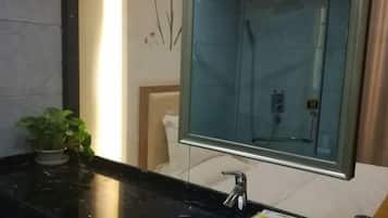 Un baño con encimera de mármol negro, lavamanos blanco, mampara de ducha de vidrio y una planta en maceta.