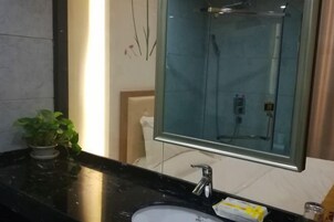 Un baño con encimera de mármol negro, lavamanos blanco, mampara de ducha de vidrio y una planta en maceta.