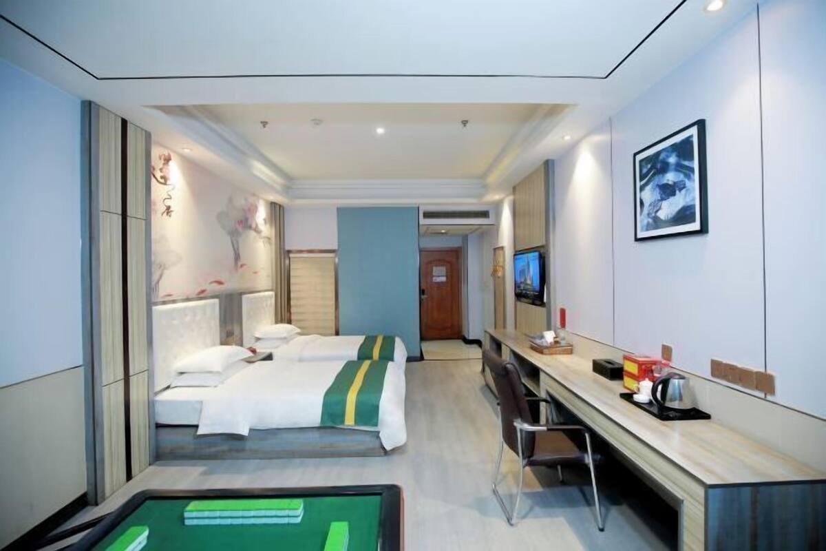 A hotel room with two beds, a desk, a chair, a television, and a bathroom door.