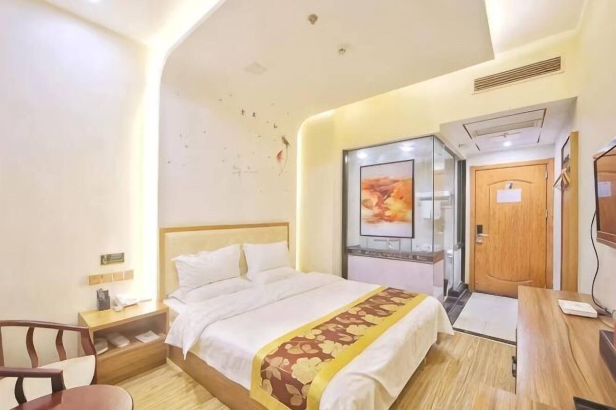A hotel room with a bed, a desk, a chair, and a door.