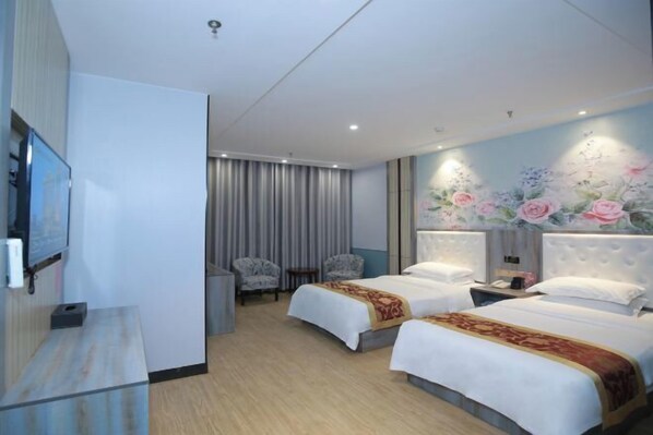 A hotel room with two beds, a TV, a desk, and a wall with floral artwork.