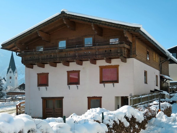 Un chalet traditionnel en bois, doté d’un balcon, de nombreuses fenêtres et surplombant un paysage enneigé.