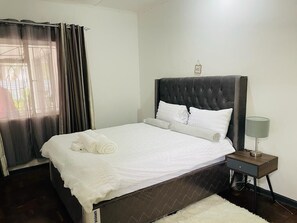 Een net opgemaakt bed met witte lakens, een donker hoofdbord en een nachtkastje met een lamp.