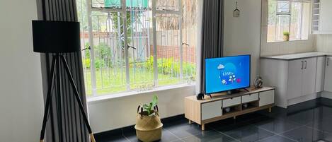 A modern living room with a large window, a flat-screen TV, a wooden cabinet, and a black floor.