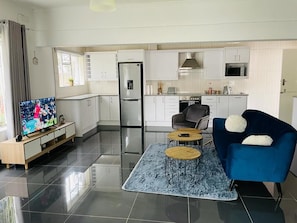 A modern living room with a TV, a blue sofa, and a kitchen area with white cabinets and appliances.