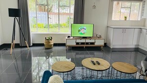 Un soggiorno moderno con televisore, due tavolini rotondi, un divano blu e un angolo cottura con pensili.