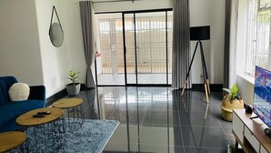 Un soggiorno moderno con un divano blu, due piccoli tavolini rotondi, un grande specchio e una televisione su un mobile in legno.