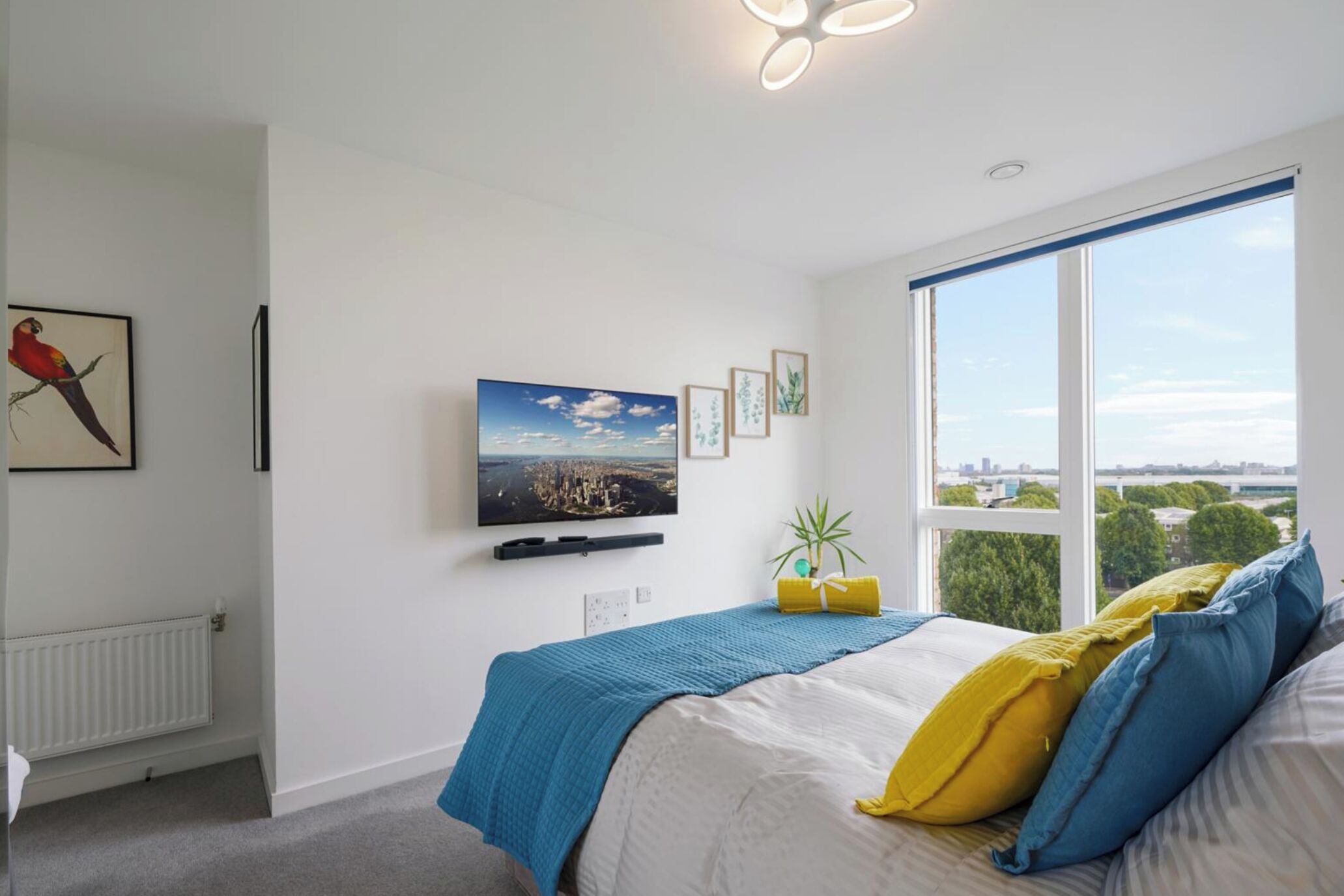 A bedroom with a bed, a TV, a window with a city view, and a radiator.