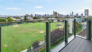 A high-rise building with a view of a cityscape, including a green field and a railway track. - Skyline View 1 Bed Apartment Sleeps 2 - Balcony (London)