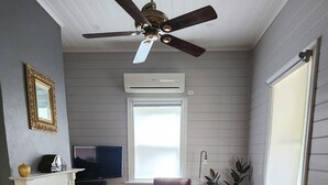 Un salon avec une cheminée, un ventilateur de plafond, un téléviseur et un canapé rouge.