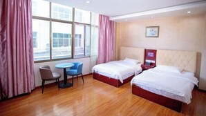 A hotel room with two beds, a small table, a chair, and large windows.