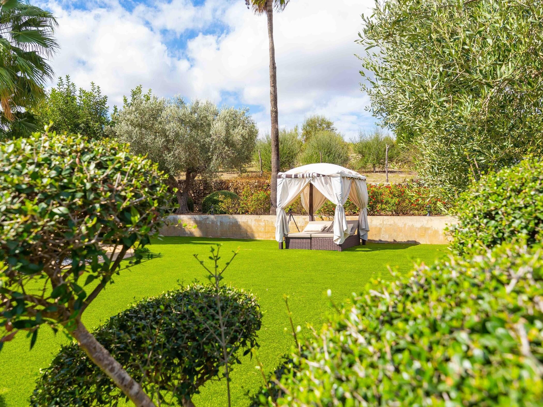 Un jardin avec un parterre d’herbe verte, un lit à baldaquin blanc et divers arbres et arbustes.