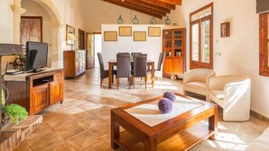 A spacious living room with a wooden ceiling, a dining area with chairs and a table, and a television on a wooden cabinet. - Beautiful villa with pool in Llubí, in the center of Mallorca. (Llubí)