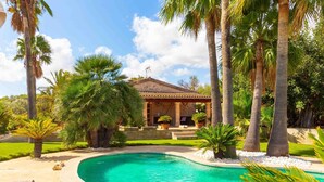A swimming pool with lounge chairs, palm trees, and a house with a tiled roof. - Beautiful villa with pool in Llubí, in the center of Mallorca. (Llubí)