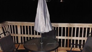 Een terras met een ronde tafel en vier stoelen, een parasol en een houten balustrade.