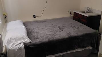 A bedroom with a bed, a flat-screen TV mounted on the wall, a small sink, and a wooden floor.
