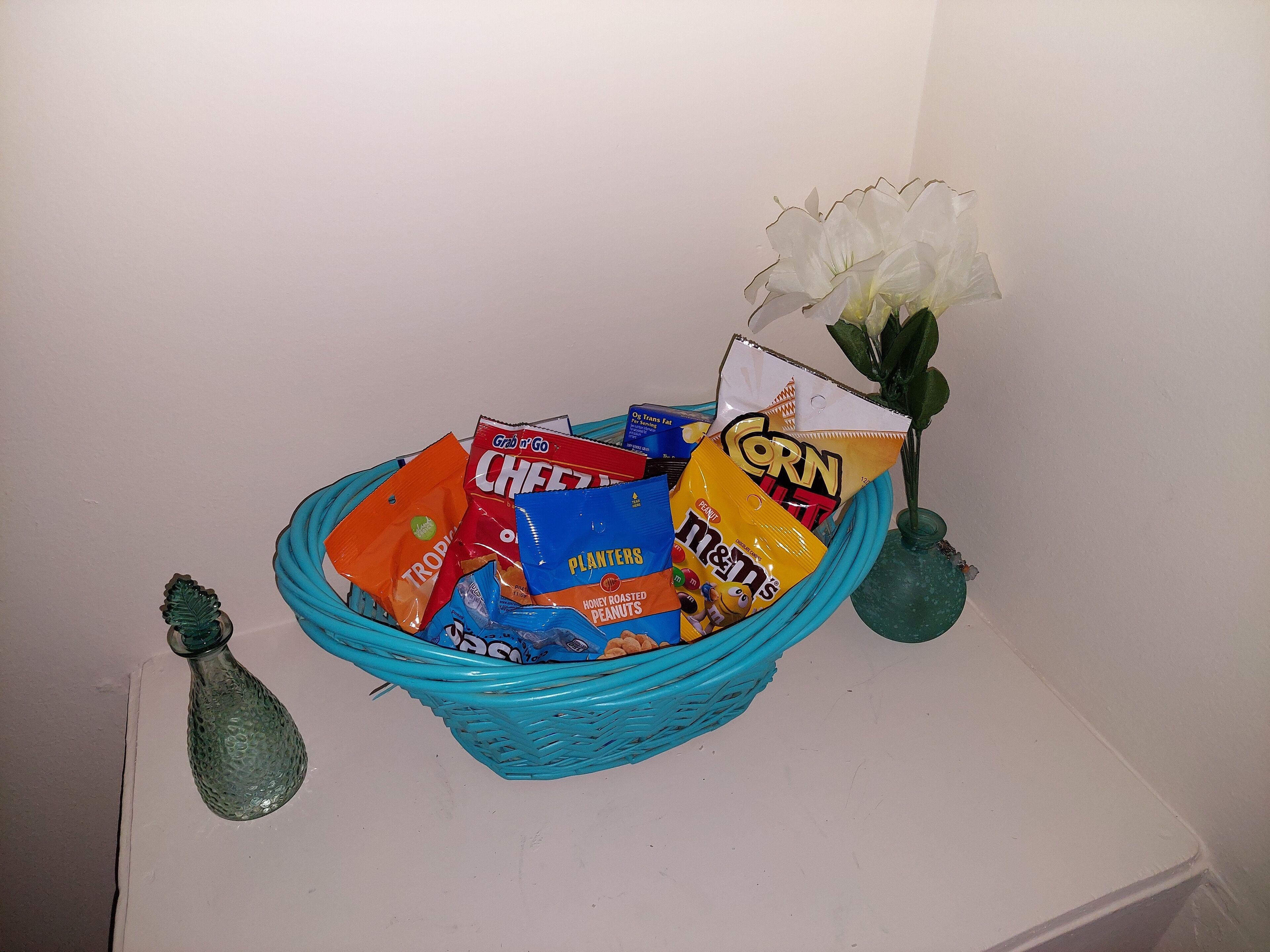 Un cesto pieno di snack e un piccolo vaso con un fiore bianco.