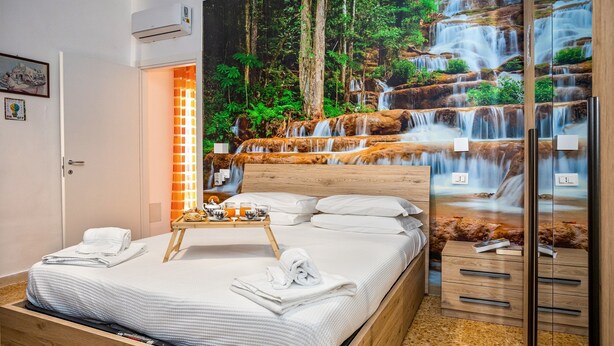 A neatly made bed with white linens, a tray with breakfast items, and a large mural of a waterfall. - B&B Sorrento Mahal Kita with unique style (Sorrento)