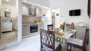 A modern kitchen with a dining area, featuring a table set for two, a microwave, and a TV mounted on the wall. - B&B Sorrento Mahal Kita with unique style (Sorrento)