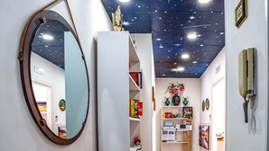 A hallway with a starry ceiling, a round mirror, a green vase with flowers, and a shelf with books and a small statue. - B&B Sorrento Mahal Kita with unique style (Sorrento)
