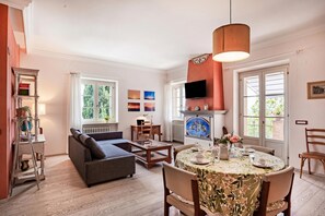 Ein Wohnzimmer mit einer Couch, einem Esstisch mit Stühlen, einem Kamin und einem an der Wand montierten Fernseher.