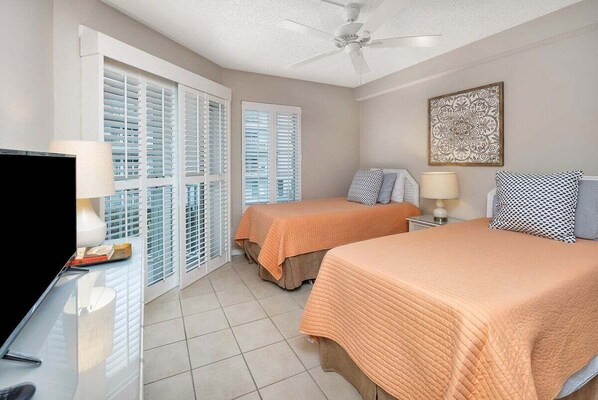 A hotel room with two beds, a television, a ceiling fan, and a window with blinds. - Oceanfront Condominium with community pool! (Saint Simons Island)