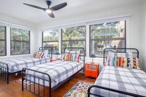 A room with two beds, each with a metal frame and plaid bedding. There is a ceiling fan, large windows, and a small orange nightstand with a lamp. - Updated 4/3 - Walk to Landa Park & Schlitterbahn! (New Braunfels)