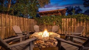 Un espacio exterior con asientos, una chimenea de piedra y sillas de madera.