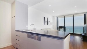 A modern kitchen with a large island, a dishwasher, and a view of the ocean through large windows. - 304 Arena Newcastle Beach (Newcastle, New South Wales, Australia)