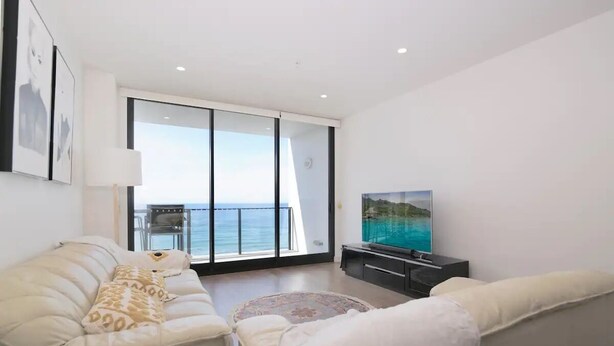 A modern living room with a sofa, a TV, and a view of the sea. - 304 Arena Newcastle Beach (Newcastle, New South Wales, Australia)