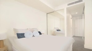 A hotel room with a large bed, a bedside table, a mirror, and a door leading to another room. - 304 Arena Newcastle Beach (Newcastle, New South Wales, Australia)
